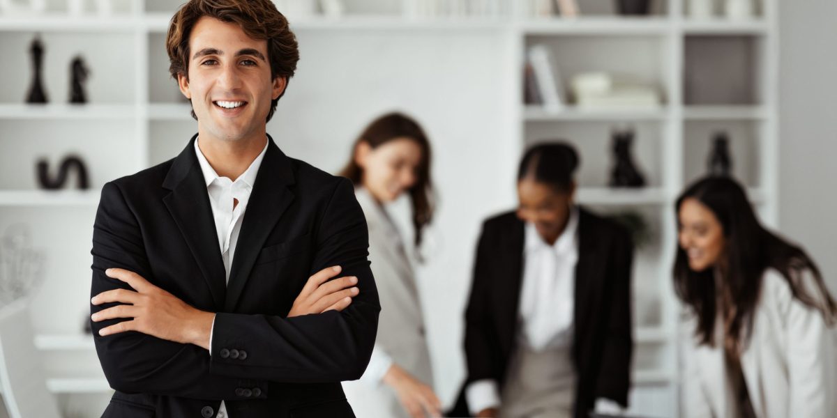 Happy european businessman in suit standing with folded arms in front of his colleagues, posing in office during meeting contratação internacional de talentos